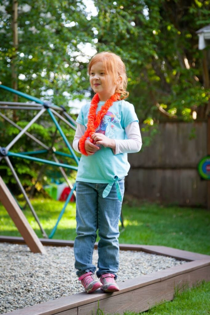 A child in a tulle necklace stands near a backyard play structure.