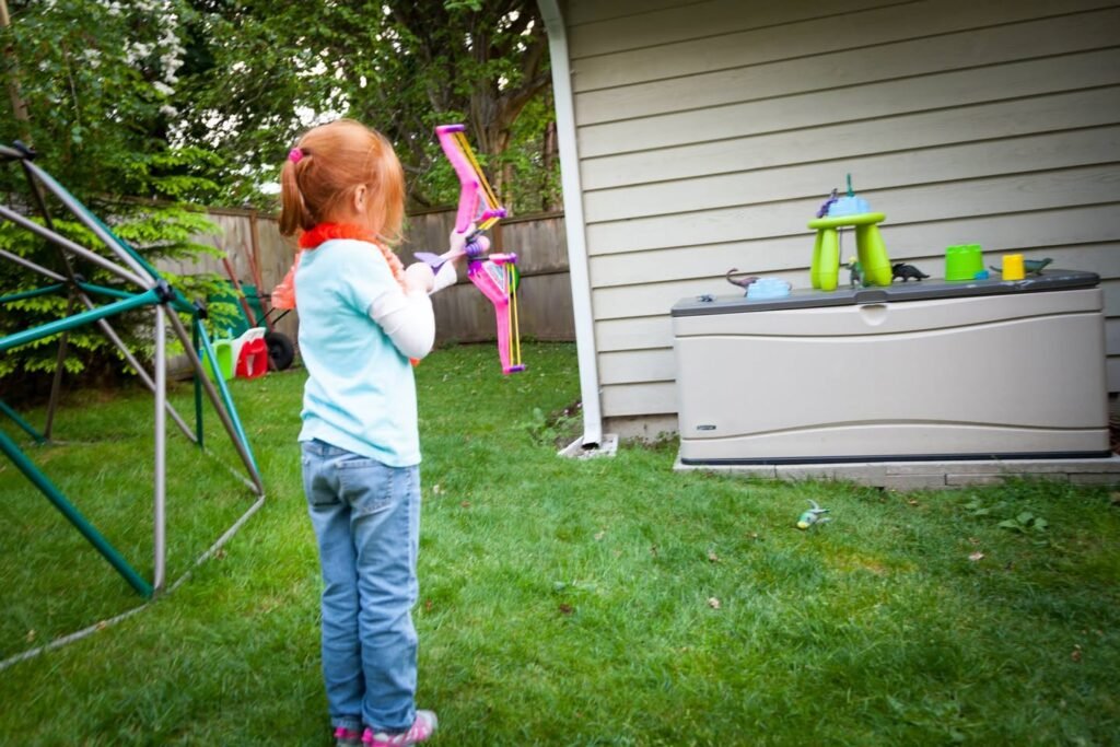 A child in a backyard holding a colorful toy bow and arrow.