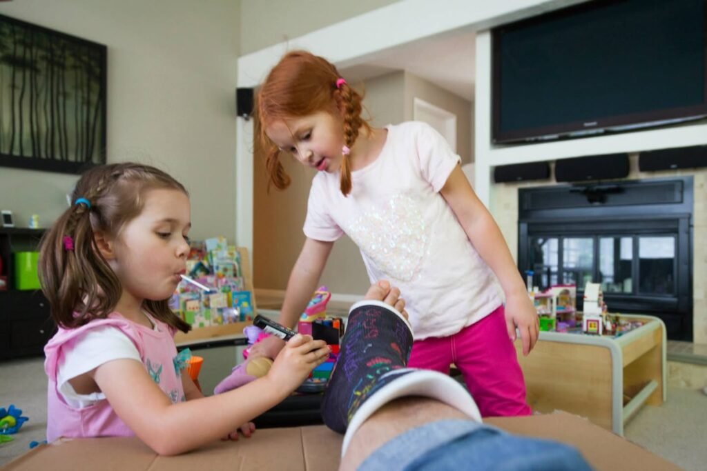 Two children are carefully decorating a shoe with markers on their lap indoors.