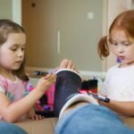 A photo of two young children using colored markers to decorate an adult's foot while at a kitchen table.