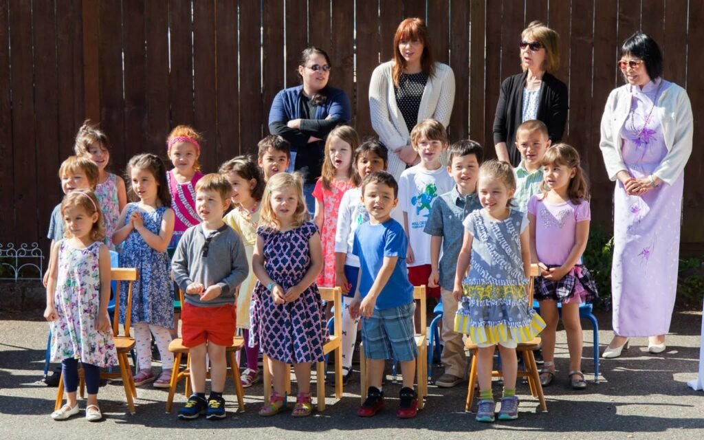A group of children and adults standing together for a photo, set against a wooden fence background.