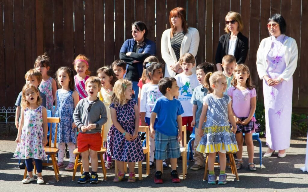 Children sing on chairs outdoors with adults standing behind, captured in four overlapping photo panels.