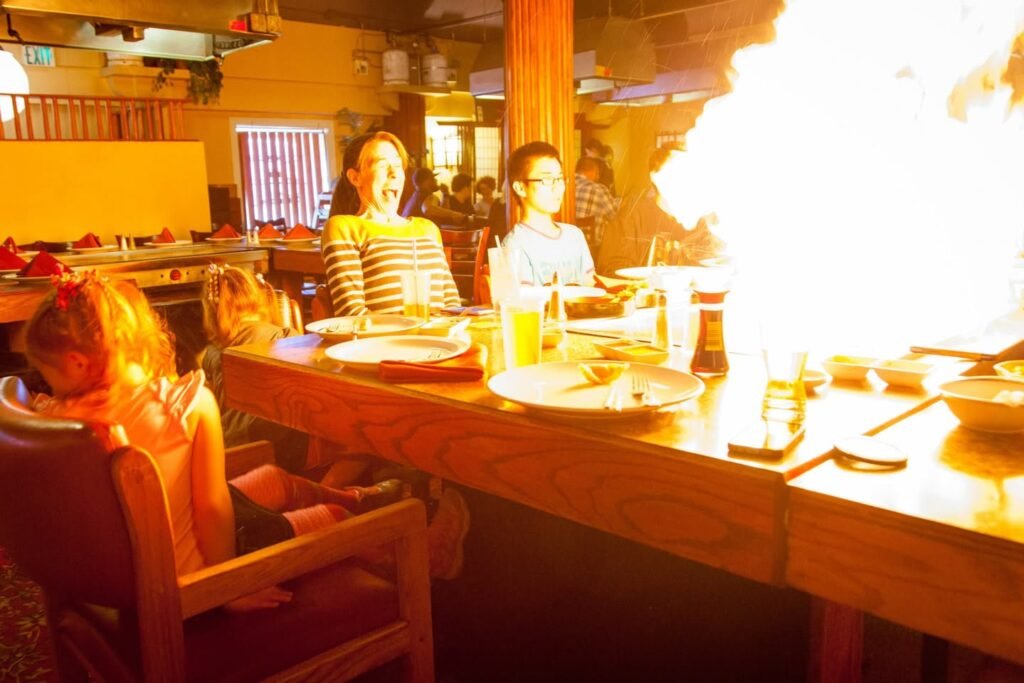 Diners enjoy a dramatic tableside flame show at a restaurant. Warm lighting highlights the wooden table and excitement of the dining group.