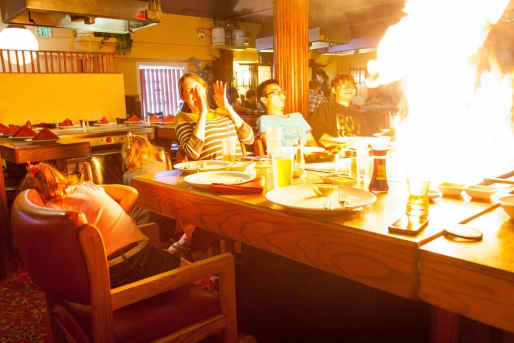 Patrons watch a dramatic fire performance at a restaurant bar counter.