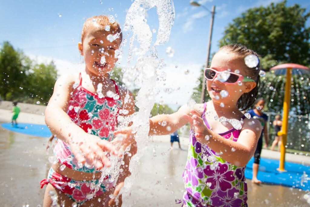Two kids in swimwear playing in a splash pad on a sunny day.