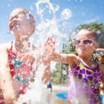 Children playing and splashing in a water park with bright blue skies and vibrant clothing.