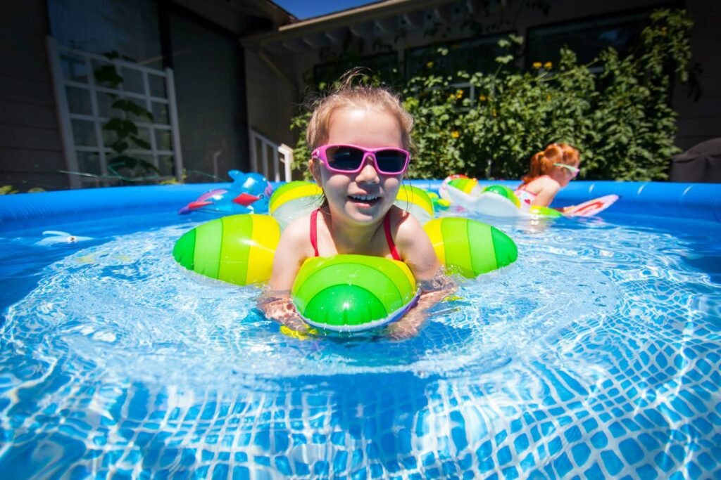 A child in pink sunglasses and a floatie enjoying a sunny day in a pool.