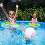 Children splashing in a blue bounce pool with colorful floats and a pink ring ball.