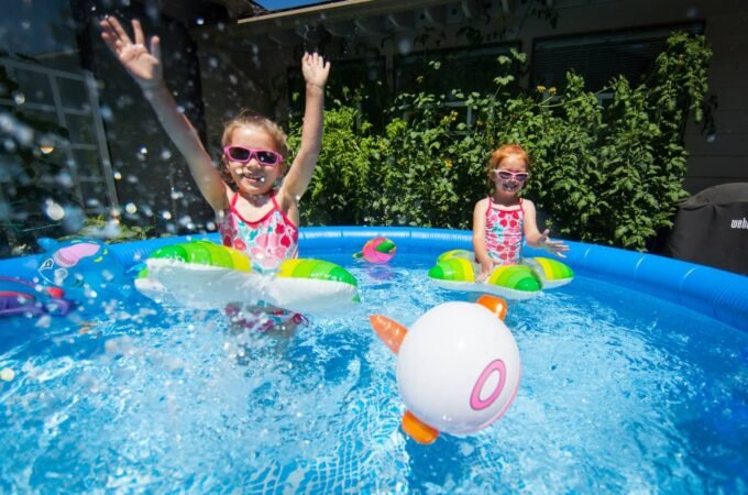 Children splashing in a blue bounce pool with colorful floats and a pink ring ball.