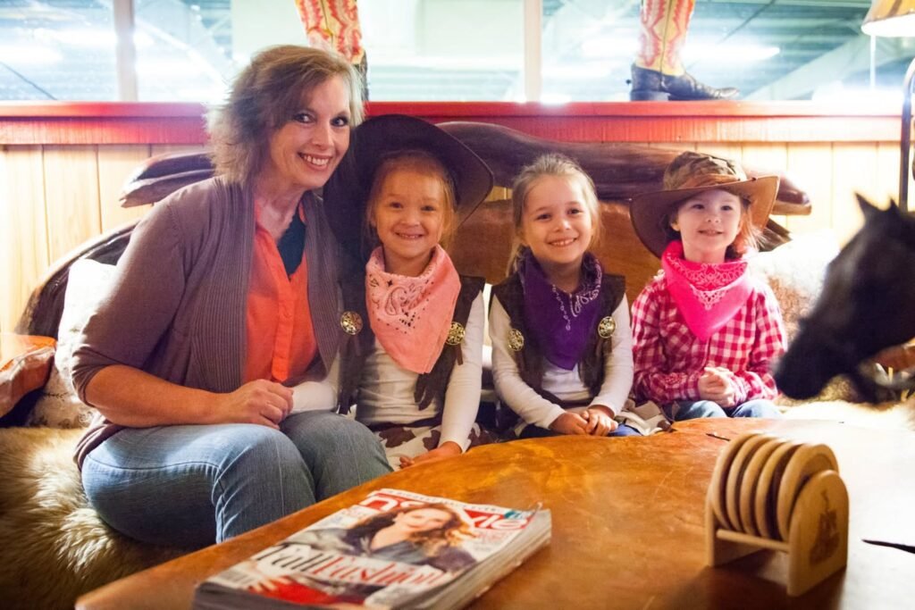 A woman and three children are seated indoors with horse-themed decor and western gear.