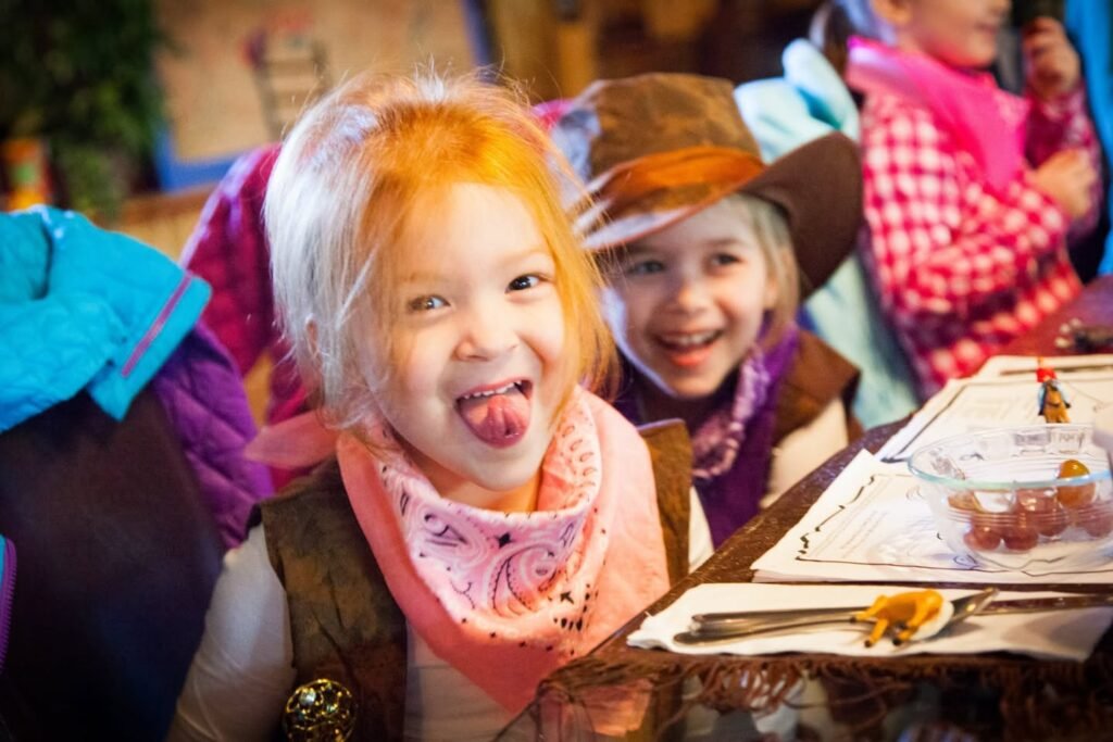A young child sticks their tongue out while another smiles nearby.
