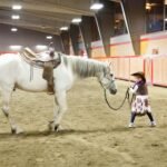 A young teenager practicing basic horse handling in an indoor arena.