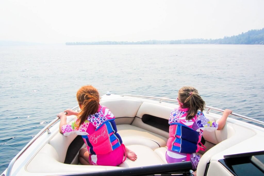 Children wearing life jackets enjoy boating on a calm body of water.