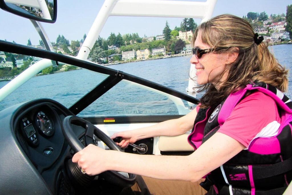 A person in a pink life jacket steers a boat on a scenic waterway.