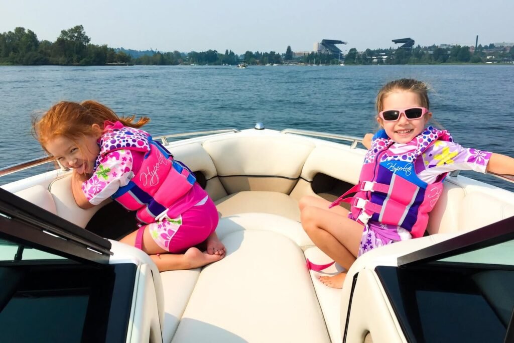 Two children wearing life jackets enjoy a boat ride on the lake during a sunny day.