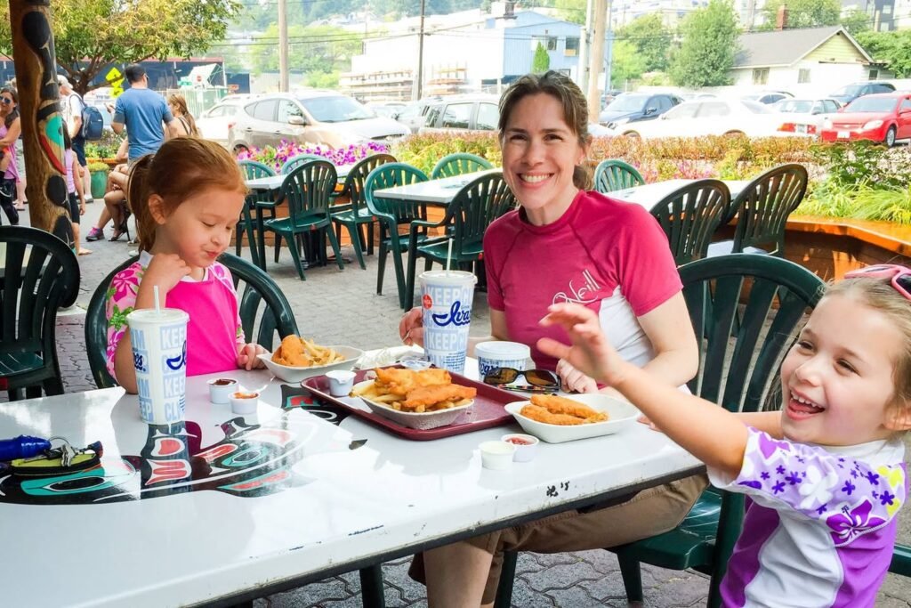 Smiling family at an outdoor table with plates of donut holes and other food under a sunny sky.