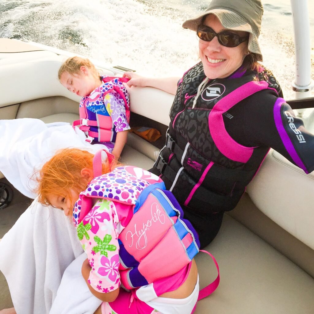 A smiling woman and two children wearing life jackets on a boat, enjoying a day out on the water.