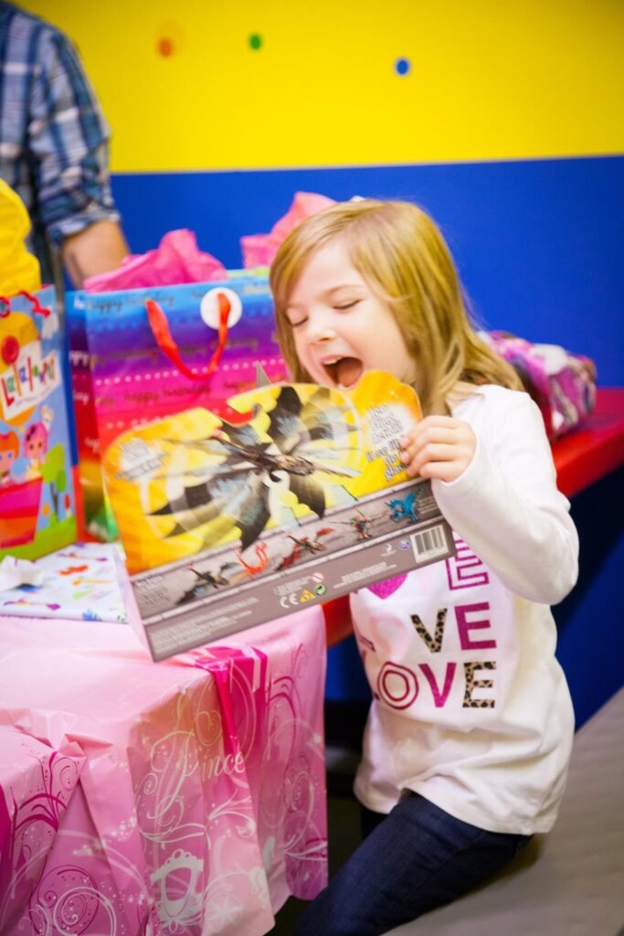 A child opens an exciting birthday gift in a colorful room. The scene is filled with bright decorations and festive energy.