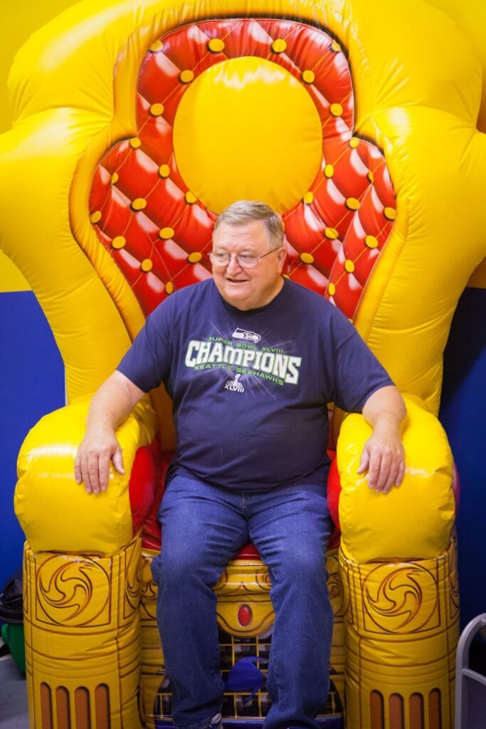 A person sits comfortably on a large yellow and red inflatable throne. The bright colors make for a playful and eye-catching scene.
