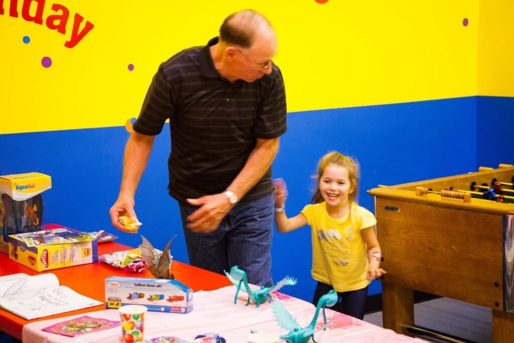 Two people enjoy games and crafts in a colorful indoor playroom. The setting includes a foosball table and a craft table with vibrant decorations.