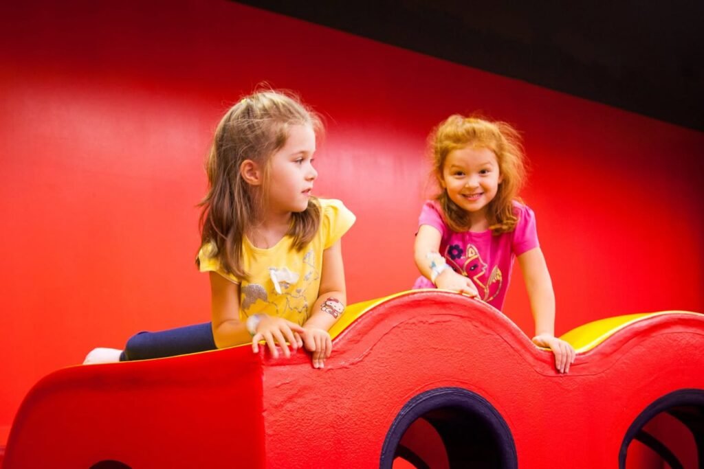 Two children enjoy time on a bright red play structure in an indoor play area.