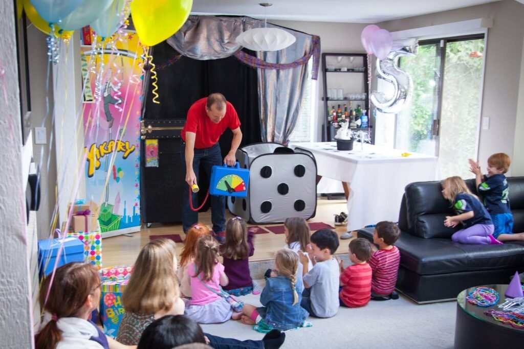 A group of children watches an adult perform with an oversized toy die and spinner at an 8th birthday party. The room is decorated with balloons, streamers, and a large number 8 balloon.