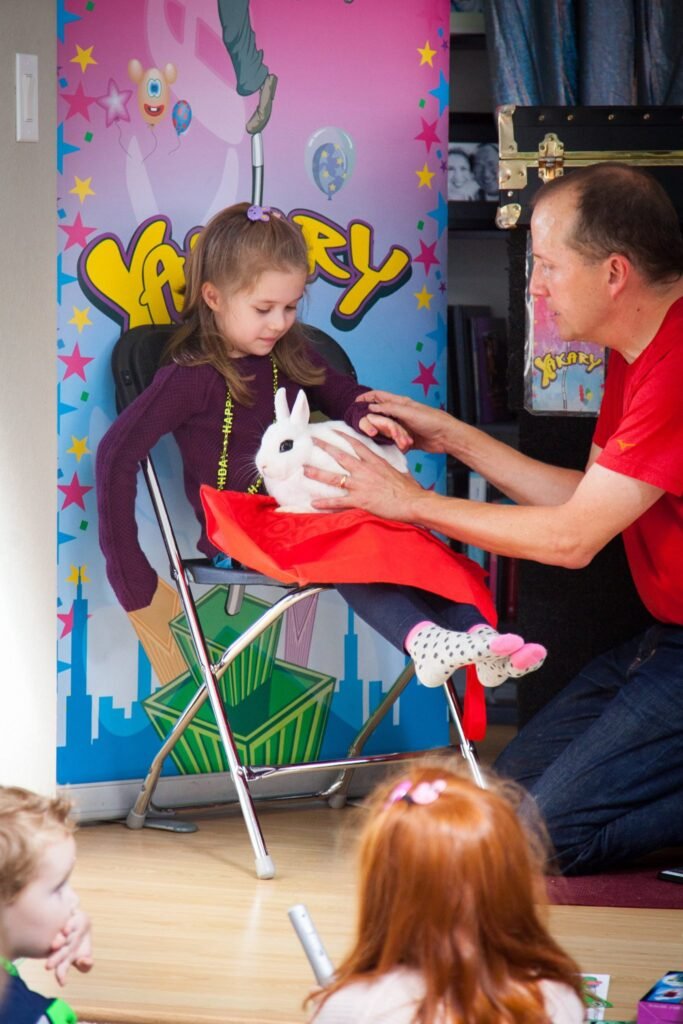 A child sits holding a white rabbit on a red cloth in front of a colorful banner.