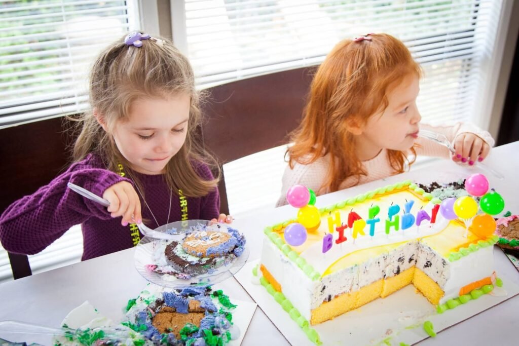 Two children at a table with a decorated birthday cake and playful snacks. A festive atmosphere with bright colors and party foods shared by family members.