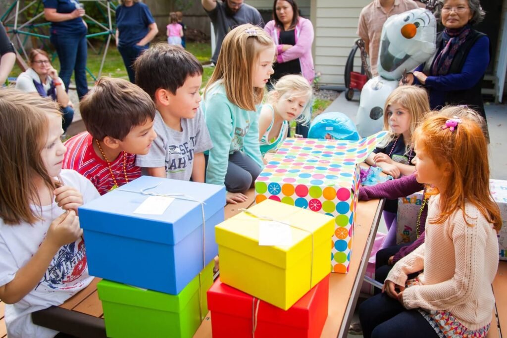 Children sitting around a table with colorful gift boxes. Family and friends gathered at an outdoor community event.