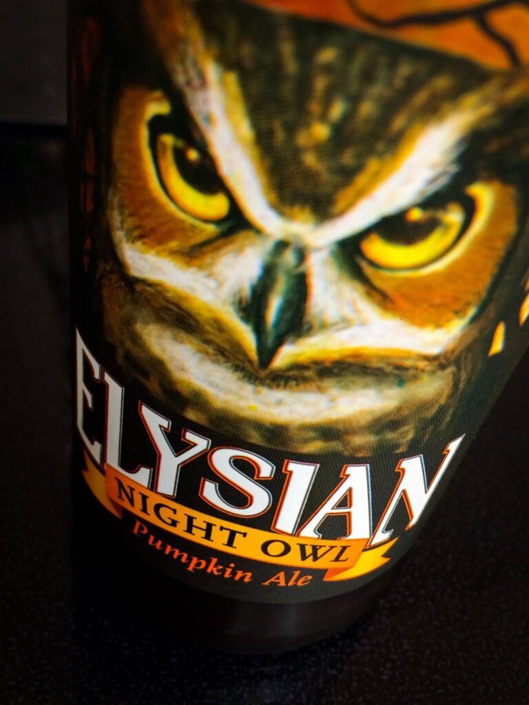 A close-up detail of an Elysian Night Owl Pumpkin Ale bottle featuring a vivid owl illustration.