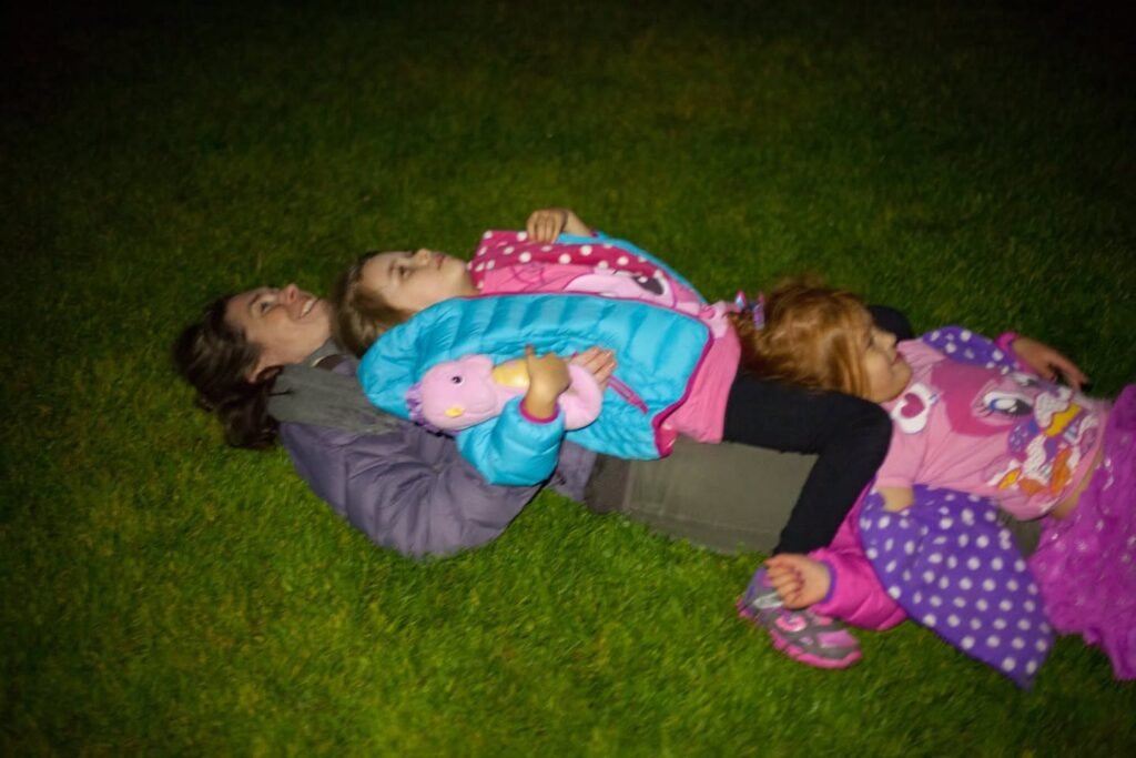A family relaxing on the grass at night. They are wrapped in colorful blankets.