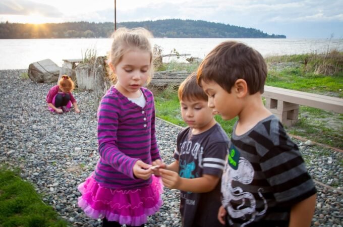 Children on a rocky lakeside path at sunset, holding small items together while a lake stretches into the distance.