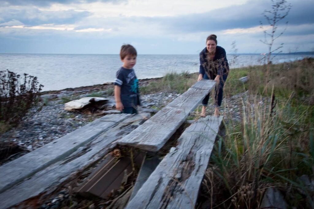 Two individuals explore a rugged coast with weathered wooden planks and a grassy shoreline.