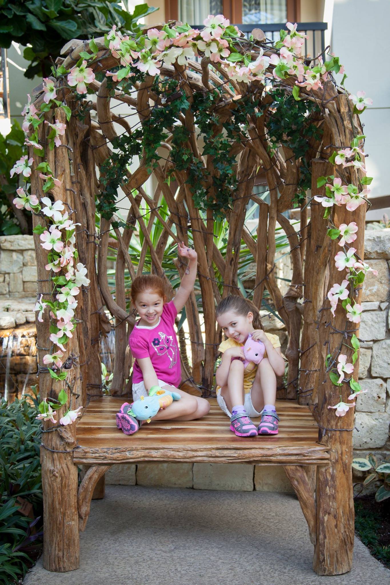 Gaylord Texan Resort Two young children sitting on a rustic wooden bench constructed from branches, decorated with climbing pink and white flowers in a garden setting.