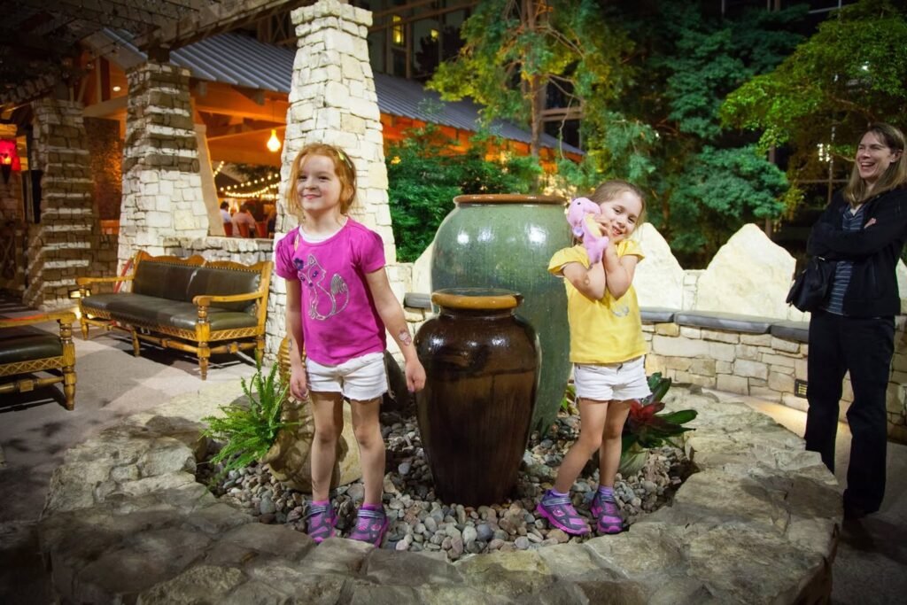 A family enjoys an evening at a rustic stone amphitheater with large ceramic pots and natural greenery.