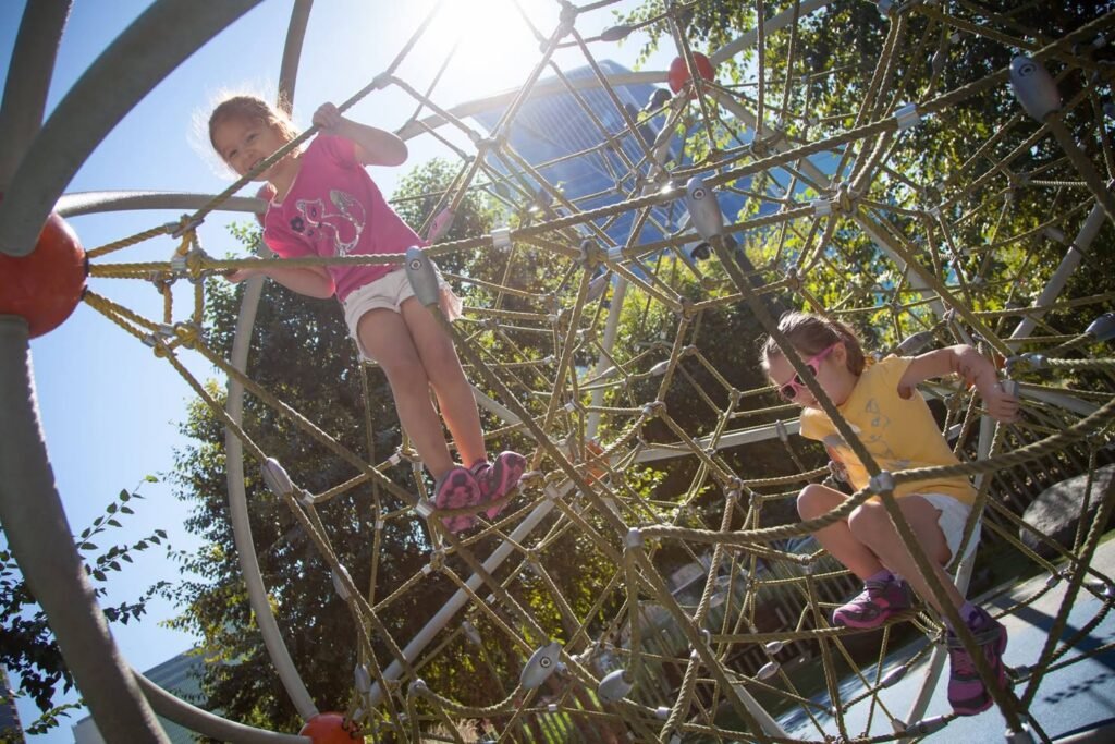 Children climbing on a large spherical playground structure under a sunlit sky.