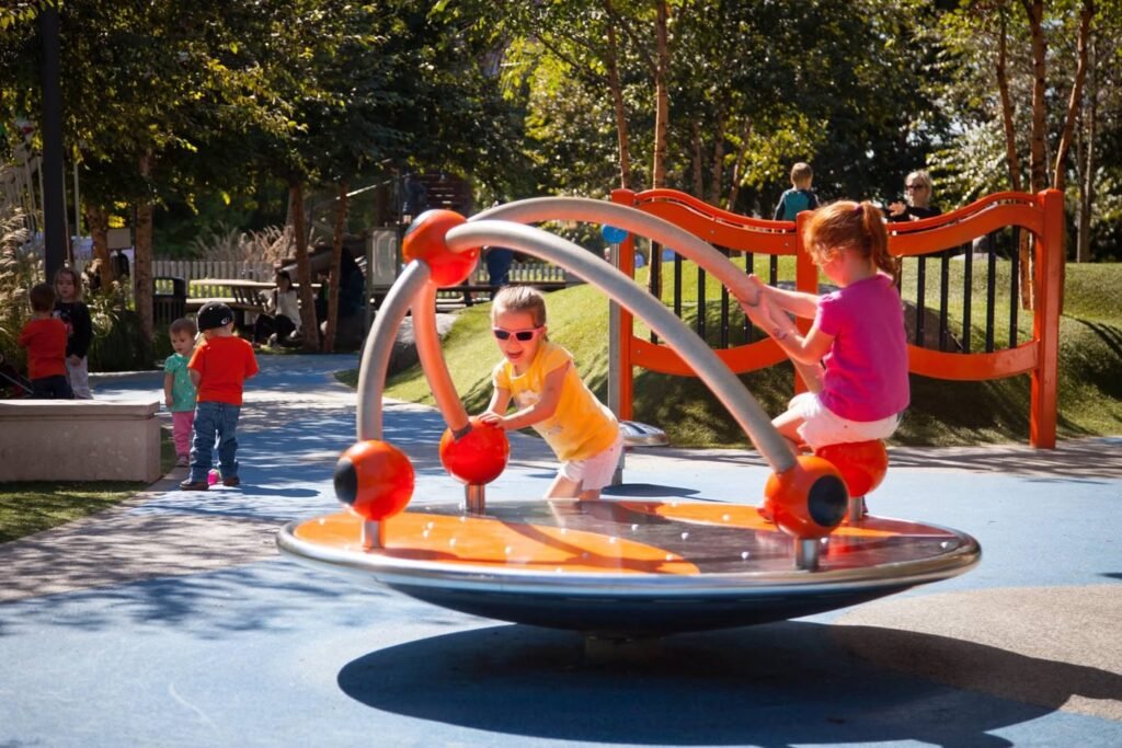 Children enjoy a sunny day at a park, playing on a spinning playground equipment.