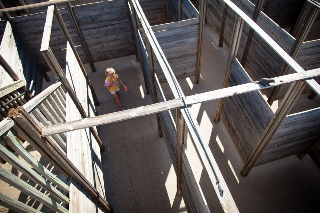 A descending view of a wooden spiral staircase with sunlight casting sharp geometric shadows on the steps and railings.