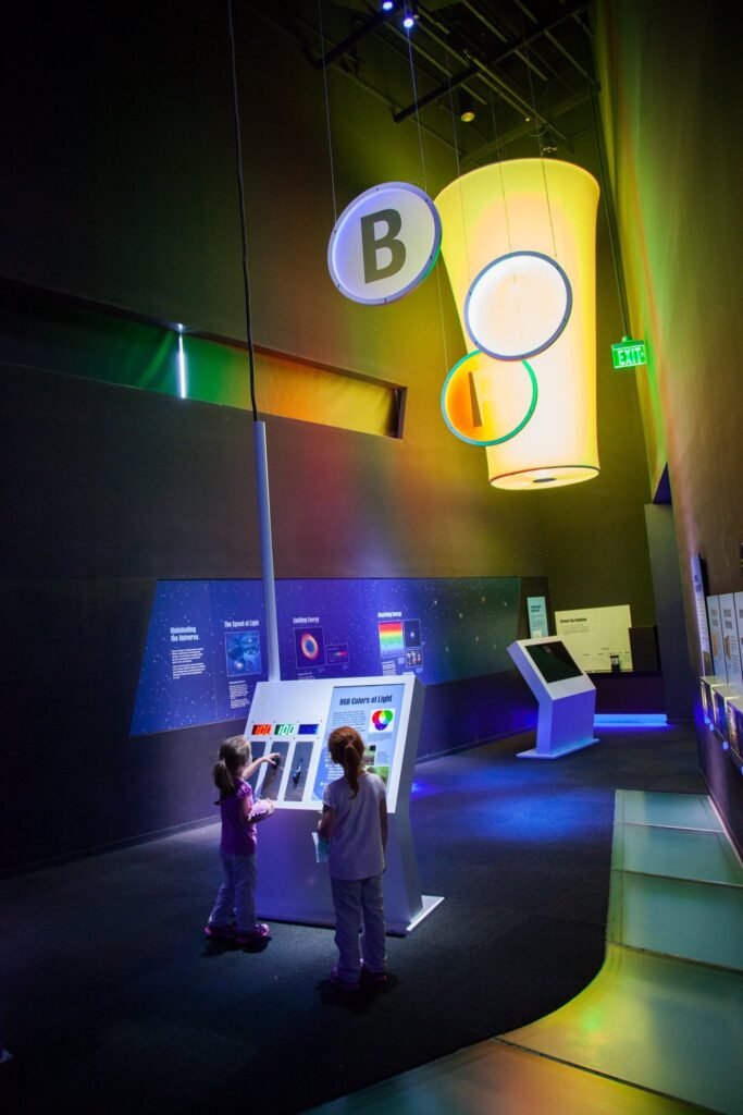 A modern museum exhibit featuring illuminated displays and interactive screens in a dimly lit gallery.
