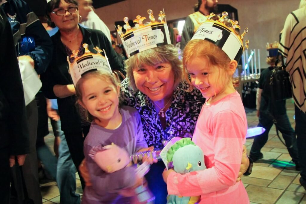 A group wearing matching letterman-style crowns at what appears to be a theater or celebration event, smiling together with stuffed animals.
