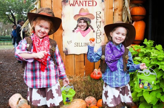 Two children in cowboy outfits at a pumpkin patch with a Wild West wanted poster and a hay bale structure.