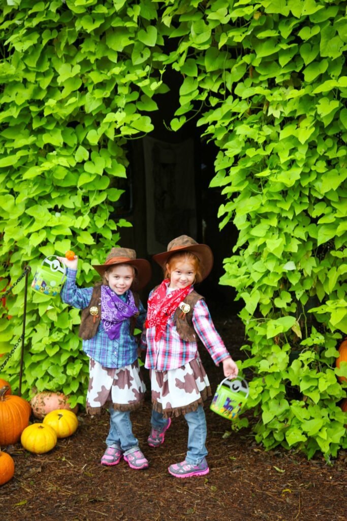 Two young people in cowboy hats and plaid shirts holding small baskets in front of a lush green vine wall.