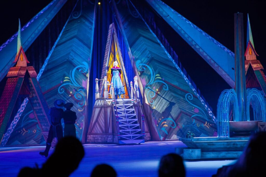 A nighttime scene of a large illuminated archway and structures with blue lights and fountains.