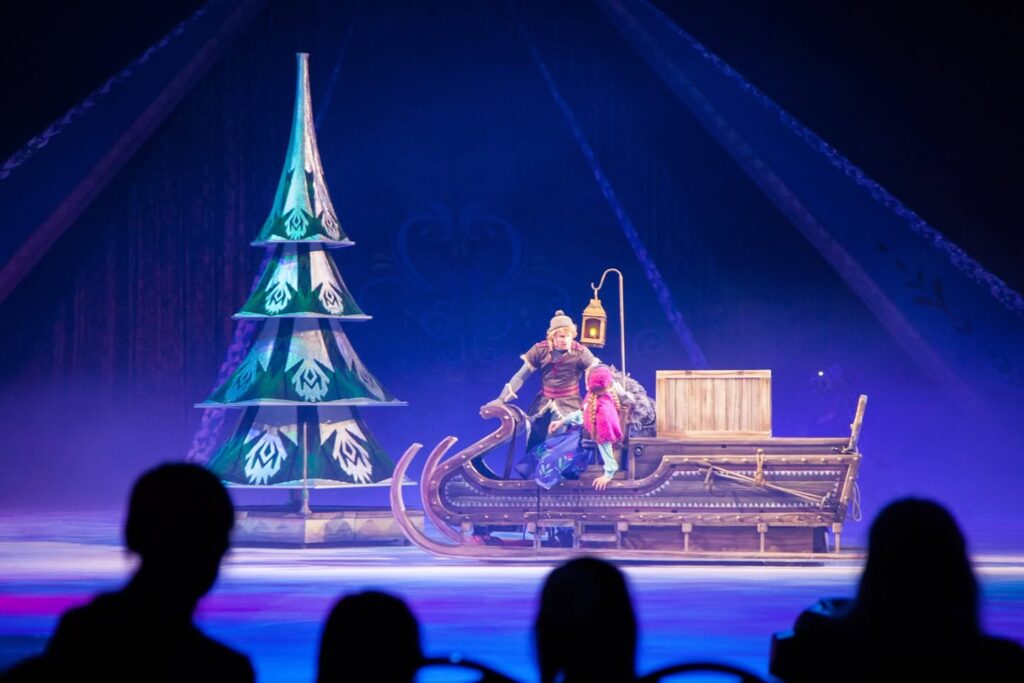 A character on a sled in front of a spire at an ice-themed show.