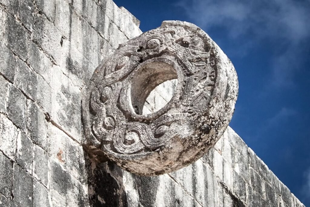 An ornate, circular stone carving is set into a weathered stone wall against a deep blue sky, showcasing ancient craftsmanship.