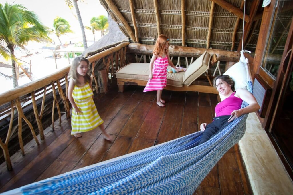 Children playing in a tropical bamboo pavilion with a hammock and palm trees in the background.