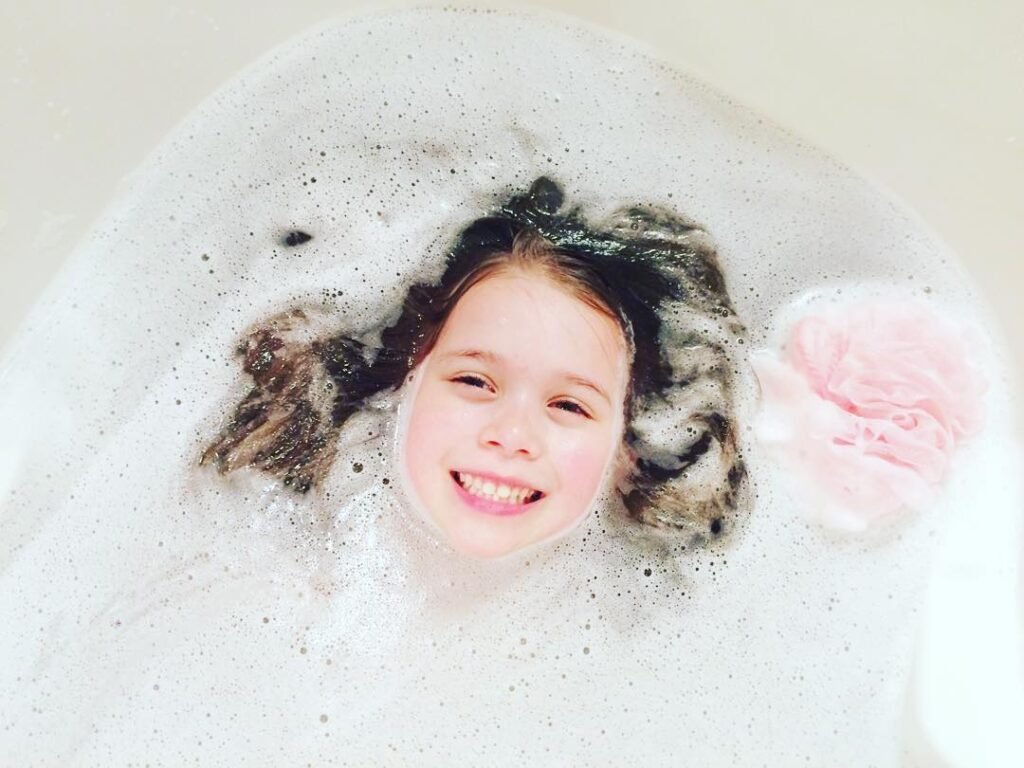 A smiling child peeks through a sea of bubbles in a warm bath. Fun and cozy moment captured at home.