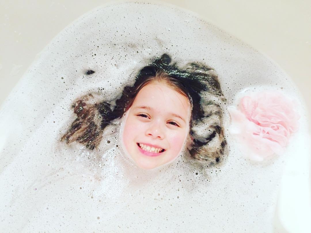 A smiling child peeks through a sea of bubbles in a warm bath. Fun and cozy moment captured at home.