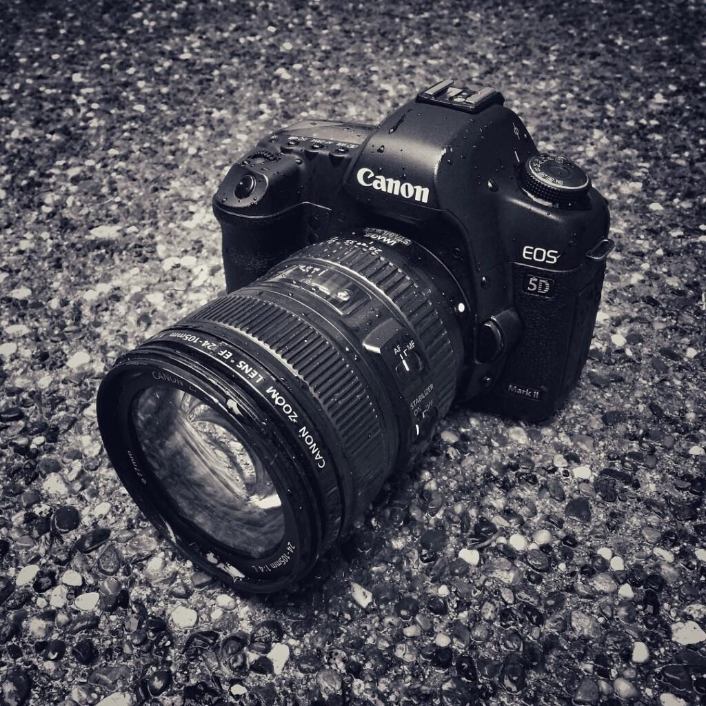A Canon EOS 50 DSLR camera with a lens resting on a textured gravel surface.