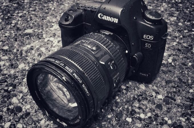 A Canon EOS 50 DSLR camera with a lens resting on a textured gravel surface.